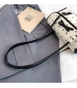 Detailed top view of a cream cylinder bag with black bows on a grey blazer background