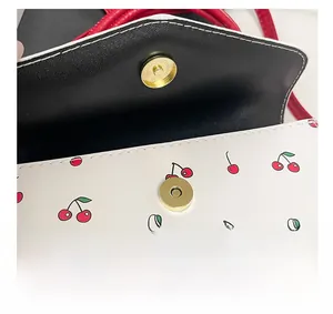Close-up of golden magnetic clasp and cherry print on white crossbody bag detail