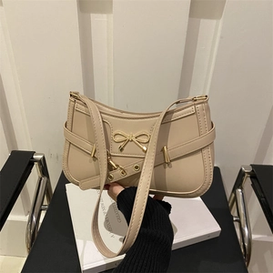 Chic beige bow baguette shoulder bag with gold hardware in a minimalist setting