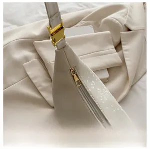 Close-up of smooth gold zipper and snake-embossed leather texture on a cream shoulder bag