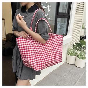 Detail of a large red and white gingham canvas tote bag held by a model in a cafe