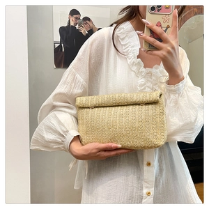 Detail of woven straw clutch bag with textured roll-edge design and natural beige finish