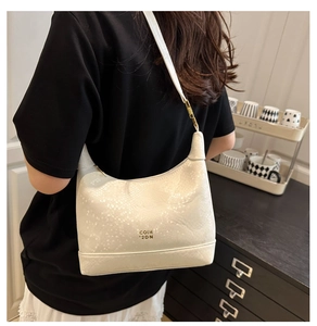 Close-up of white shoulder bag with snake skin texture and gold logo on the front