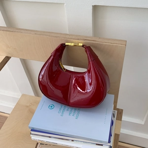 Sac hobo croissant élégant en cuir verni bordeaux avec détails dorés sur une table