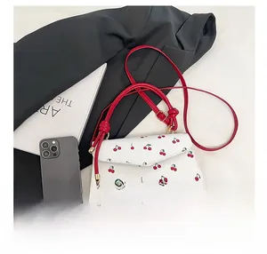 Close-up of white crossbody bag with red cherry print and vibrant red shoulder strap