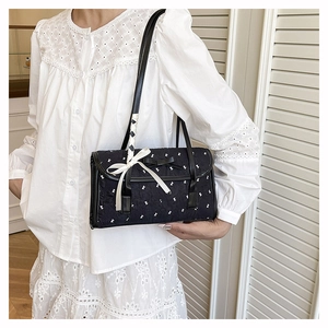 Detail of black bow handbag with white ribbon and quilted texture shown on person