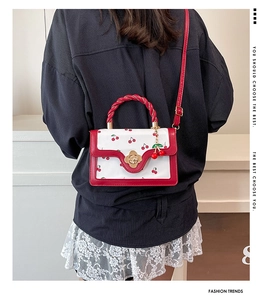 Detail of red cherry print bag featuring a woven handle and floral metal clasp closure
