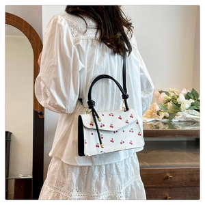 Detailed view of white cherry print handbag with knotted black handle and gold hardware
