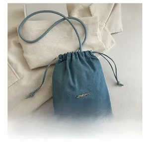 Mini sac seau en denim avec cordon de serrage et logo en métal comparé à un smartphone