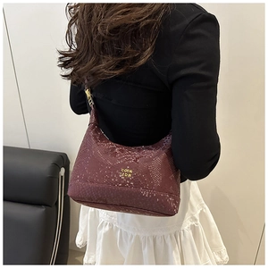 Deep burgundy dumpling bag with python texture shown on a shoulder for daily style