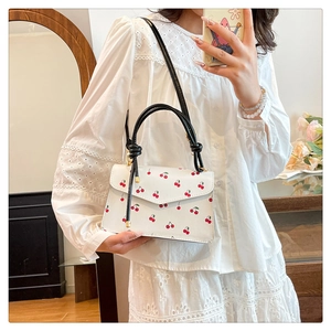 Detailed view of white cherry print handbag with golden hardware and black handles
