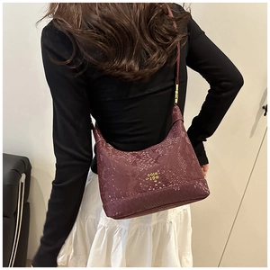 Detailed view of dark purple snakeskin texture and metal logo on shoulder bag