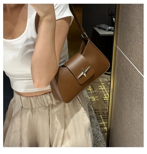 Detail of a brown underarm bag with a silver cross-star buckle on high-quality leather