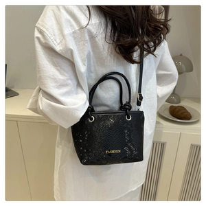 Detailed view of black snake-embossed bucket bag with gold 'FASHION' lettering on model