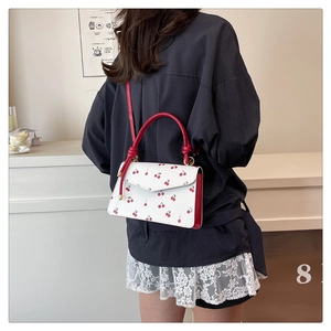 Detail of white leather shoulder bag with cherry print and red straps worn by a model