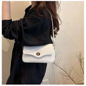 Détail d'un sac à main blanc minimaliste avec un fermoir rotatif métallique doré rond