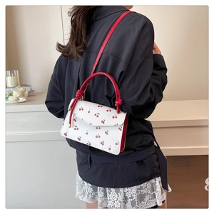 Detail of white leather crossbody bag with cherry pattern and red handle on a model
