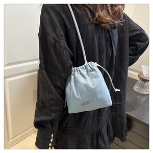 Detail of light blue denim drawstring bucket bag with metal logo and shoulder strap