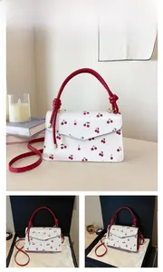 Detail of red cherry print bag with cylinder handle and gold hardware on white leather