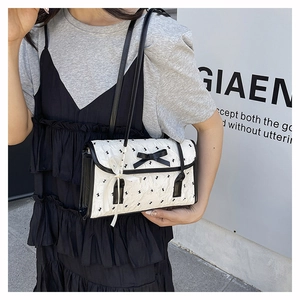 Detail of white quilted shoulder bag with black bows and floral prints worn by a model