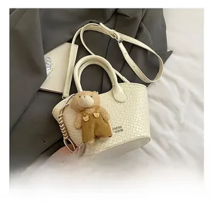Détail du sac seau tressé crème avec bandoulière amovible et petit pendentif d'ours