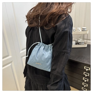 Detail of light blue denim bucket bag with drawstring strap and gold lettering logo