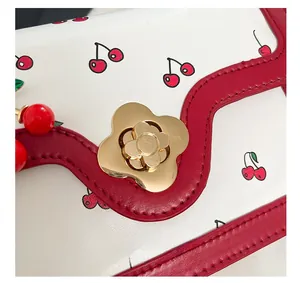 Macro detail of golden flower metal clasp on cherry print crossbody bag with red trim