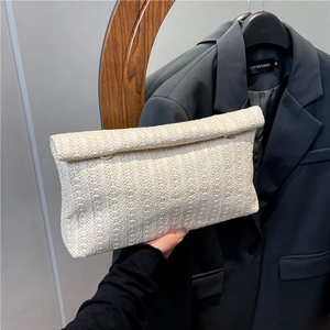 Minimalist beige woven clutch bag with flap design shown in hand for elegant style