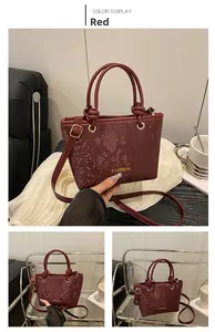 Detail of burgundy snakeskin embossed PU leather handbag with gold metal rings and top handle