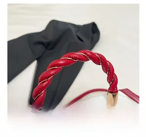 Detail of red woven leather handle and cherry print on white crossbody bag with gold hardware