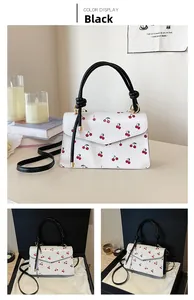 Detailed view of white cherry print handbag with black handle in a cozy home setting