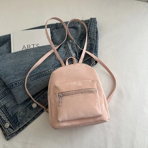 Detail of pink faux suede backpack with embossed logo next to an arts book and denim jacket