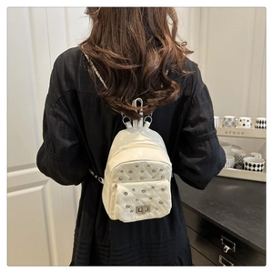 Rear view of a white quilted mini backpack with rivets and silver chain strap on a model