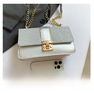 Close-up of silver sequin square crossbody bag with gold chain and smartphone for scale