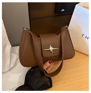 Détail d'un sac porté épaule en cuir marron avec une boucle en étoile argentée