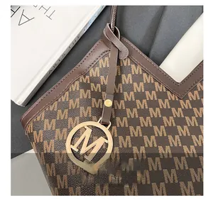 Close-up of brown monogram tote bag featuring a decorative gold metal M pendant