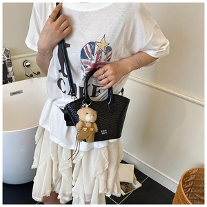 Détail du sac à main tissé noir avec logo texte blanc et breloque ours brun en peluche