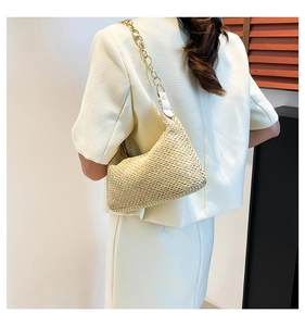 Detail of woven straw tote bag with chunky gold chain strap and white leather fasteners