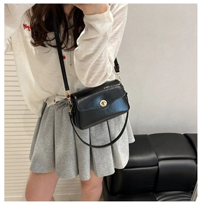 Detail of black glossy square crossbody bag with gold twist lock on female model