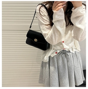 Model wearing a black matte leather square bag with golden buckle and grey pleated skirt