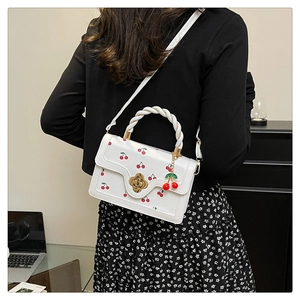 Détail du sac à main blanc à motif cerise avec poignée tressée et fermoir fleur doré