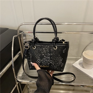 Fashion black snake print tote bag with metal logo held against modern studio backdrop