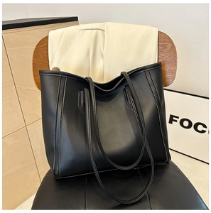 Detail of a black leather tote bag with dual shoulder straps and fine textured finish