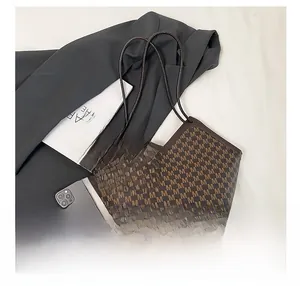 Close-up of brown monogram tote bag with gold M-shaped charm and slim leather handles