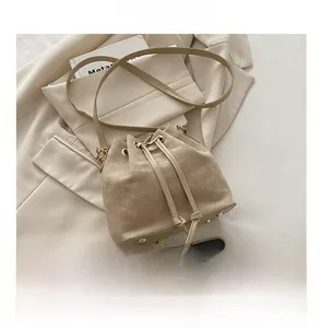 Detail of beige bucket bag with drawstring closure and metal feet next to a smartphone