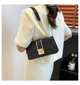 Detail of a chic black square crossbody bag with glitter texture and gold chain strap