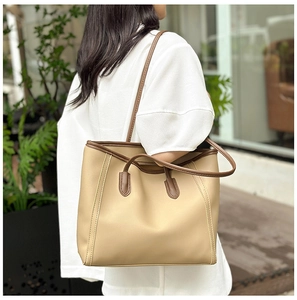 Detail of a large beige tote bag with brown straps and dual handle design in use