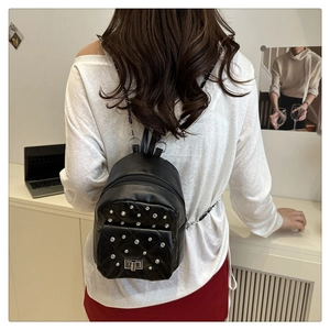 Detail of a black quilted mini backpack with silver rivets and metal chain strap on model