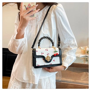 Detail of cherry print handbag with woven handle and gold flower buckle on white lace shirt