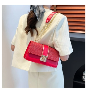 Detail of red glitter and leather crossbody bag with gold lock and chain strap on model